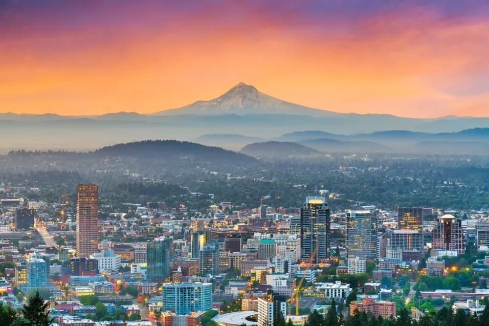 Portland city lights at sunset with Mount Hood on the horizon, illustrating the executive car run from Portland to Bend for RDM Airport, Sunriver Resort, Deschutes Brewery and the Old Mill District