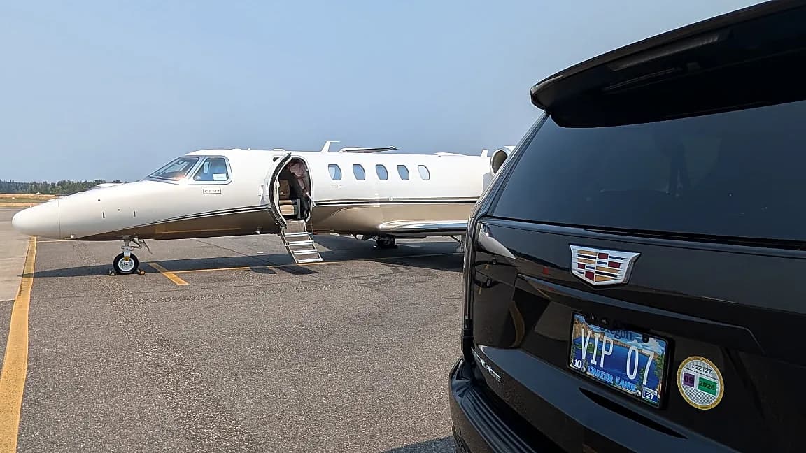 Rear of a Cadillac Escalade beside a private jet on the ramp — private aviation chauffeur transfer