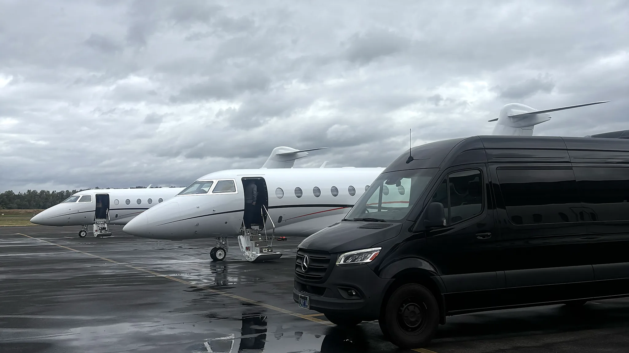 Mercedes-Benz Sprinter beside a private jet on a wet ramp — FBO group transfer for crews and parties